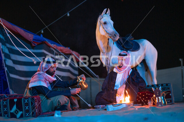 صب القهوة باستخدام الدلة النحاسية، مفهوم كرم الضيافه والاستقبال، جلسات شعبية داخل خيمة تراثية، عادات وتقاليد سعودية اصيلة في تقديم القهوة العربية، شغف تربية الخيول الاصيلة، صديقان عربيان خليجيان سعوديان يرتديان الشماغ والبشت يقضيان اوقات ممتعة في كشتة بر شبابية