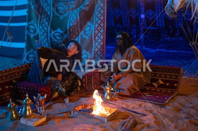 التقاط صور السيلفي التذكارية، عادات وتقاليد سعودية أصيلة في تقديم القهوة العربية، حسن الكرم والضيافة، إشعال موقد النار أثناء التخييم في الصحراء، كشتة بر في الأجواء الشتوية الهادئة، سيدتان عربيتان خليجيتان سعوديتان ترتديان الفروة تجلسان داخل خيمة شعبية تراثية