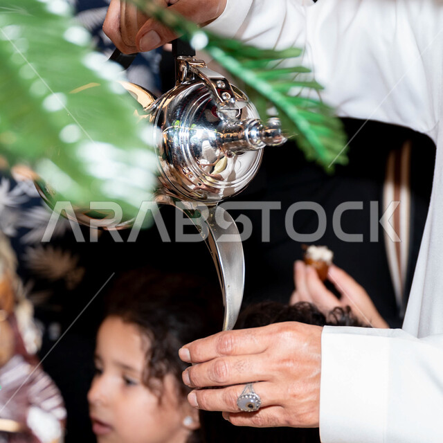 العادات التقليديه في السعوديه, صورة مقربة ليد رجل عربي خليجي يقوم بتقديم المشروبات الساخنة في الاحتفالات و المناسبات الوطنية الشعبية, دلال قهوة عربية مع فناجين زجاجي, جوده المنتجات المحليه, ضيافة اليوم الوطني السعودي 23 سبتمبر