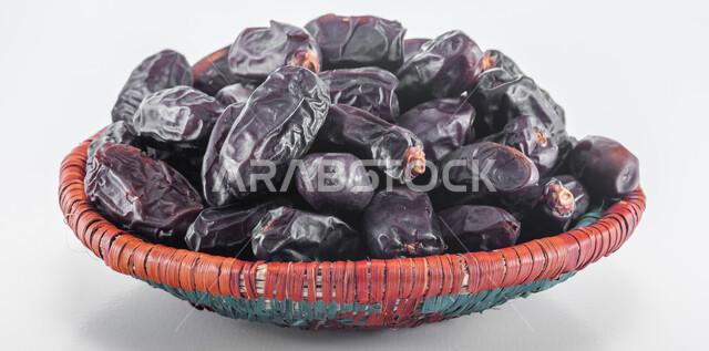 Delicious Ramadan hospitality, different types of delicious, healthy dates, healthy and beneficial food, a highly important nutritional meal, national Saudi local products, a close-up of a straw plate filled with black dates, a white background.
