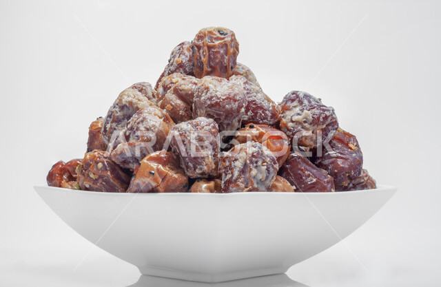 الأنواع المختلفة من التمور الصحية اللذيذة، غذاء صحي ومفيد، وجبة غذائية ذات أهمية عاليه، منتجات محلية سعودية وطنية، صورة مقربة لطبق أبيض مليء بحبات التمر المغطاة بالبذور والمكسرات، ضيافة رمضانية شهية، خلفية بيضاء 
