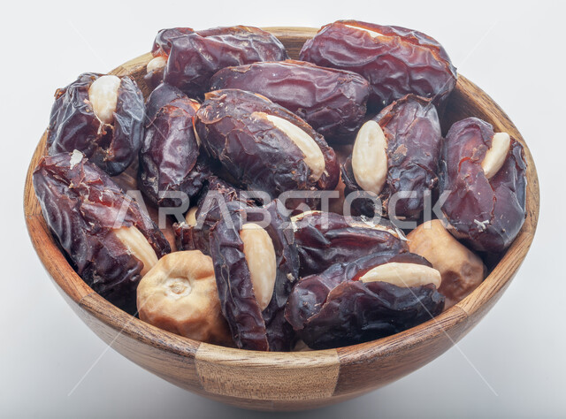الأنواع المختلفة من التمور الصحية اللذيذة، غذاء صحي ومفيد، وجبة غذائية ذات أهمية عاليه، منتجات محلية سعودية وطنية، صورة مقربة لطبق خشبي مليء بحبات التمر المحشوة بالمكسرات، ضيافة رمضانية شهية، خلفية بيضاء 