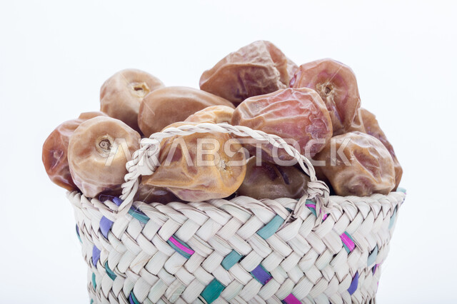 حصاد النخيل في مزارع المملكة، ضيافة رمضانية شهية، الأنواع المختلفة من التمور الصحية اللذيذة، وجبة غذائية صحية ذات أهمية عاليه، منتجات محلية سعودية وطنية، صورة مقربة لحبات التمر في سلة من القش، خلفية بيضاء 