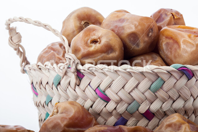 حصاد النخيل في مزارع المملكة، ضيافة رمضانية شهية، الأنواع المختلفة من التمور الصحية اللذيذة، وجبة غذائية صحية ذات أهمية عاليه، منتجات محلية سعودية وطنية، صورة مقربة لحبات التمر في سلة من القش، خلفية بيضاء 