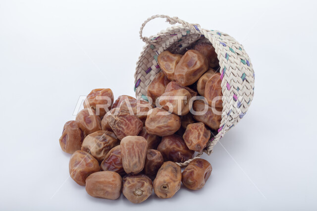 حصاد النخيل في مزارع المملكة، ضيافة رمضانية شهية، الأنواع المختلفة من التمور الصحية اللذيذة، وجبة غذائية صحية ذات أهمية عاليه، منتجات محلية سعودية وطنية، صورة مقربة لحبات التمر في سلة من القش، خلفية بيضاء 