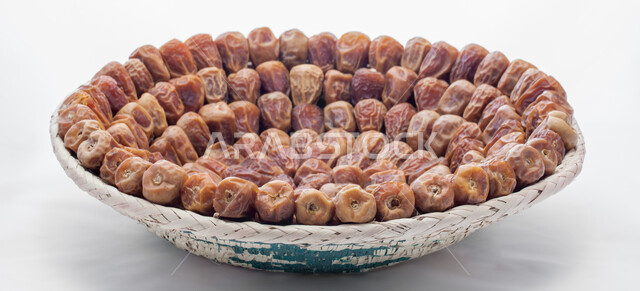 صورة مقربة لحبات التمر في طبق من القش، منتجات محلية سعودية وطنية، حصاد النخيل في مزارع المملكة، ضيافة رمضانية شهية، الأنواع المختلفة من التمور الصحية اللذيذة، وجبة غذائية صحية ذات أهمية عاليه، خلفية بيضاء 