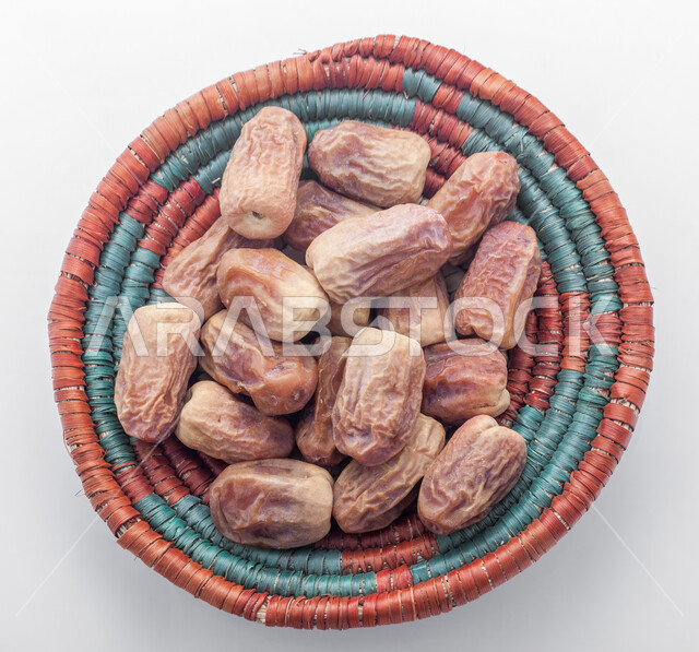 صورة مقربة لحبات التمر في طبق من القش، منتجات محلية سعودية وطنية، حصاد النخيل في مزارع المملكة، ضيافة رمضانية شهية، الأنواع المختلفة من التمور الصحية اللذيذة، وجبة غذائية صحية ذات أهمية عاليه، خلفية بيضاء 