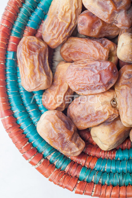 صورة مقربة لحبات التمر في طبق من القش، منتجات محلية سعودية وطنية، حصاد النخيل في مزارع المملكة، ضيافة رمضانية شهية، الأنواع المختلفة من التمور الصحية اللذيذة، وجبة غذائية صحية ذات أهمية عاليه، خلفية بيضاء 