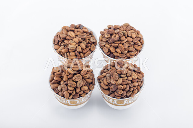 اعداد وتحضير القهوة الطازجة، جودة الصناعات والمحاصيل الغذائية الوطنية في المملكة العربية السعودية، صورة مقربة لفناجين ممتلئة  ببذور وحبات البن المحمصة باللون البني، صنع المشروبات الساخنة  اللذيذة من حبوب البن، خلفية بيضاء.