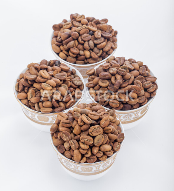 اعداد وتحضير القهوة الطازجة، جودة الصناعات والمحاصيل الغذائية الوطنية في المملكة العربية السعودية، صورة مقربة لفناجين ممتلئة  ببذور وحبات البن المحمصة باللون البني، صنع المشروبات الساخنة  اللذيذة من حبوب البن، خلفية بيضاء.
