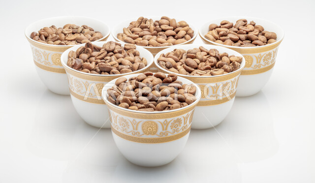 اعداد وتحضير القهوة الطازجة، جودة الصناعات والمحاصيل الغذائية الوطنية في المملكة العربية السعودية، صورة مقربة لفناجين ممتلئة  ببذور وحبات البن المحمصة باللون البني، صنع المشروبات الساخنة  اللذيذة من حبوب البن، خلفية بيضاء.