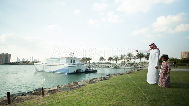 Relaxing and taking a walk in the open air, enjoying a walk on the seaside promenade, spending enjoyable times in one of the public parks, a close-up photo of an Arab Gulf Emirati man holding his daughter’s hand and contemplating the natural scenery, the concept of fatherhood and sonship, the background of nature