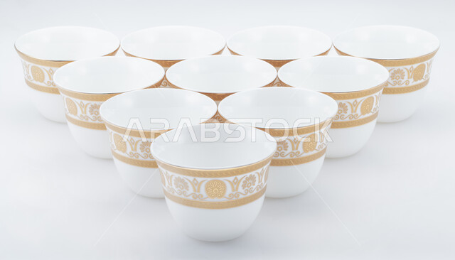 فنجان ضيافة صغير، اكواب بيضاء مزخرفة باللون الذهبي ، صورة مقربة لمجموعة من الفناجين الصغيرة، أكواب زجاجية صغيرة لتقديم المشروبات الساخنة، خلفية بيضاء