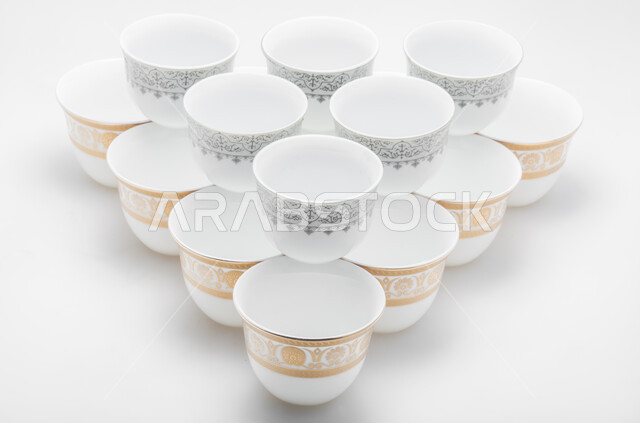 اكواب بيضاء مزخرفة باللون الذهبي والفضي، صورة مقربة لمجموعة من الفناجين الصغيرة، فنجان ضيافة صغير، أكواب زجاجية صغيرة لتقديم المشروبات الساخنة، خلفية بيضاء