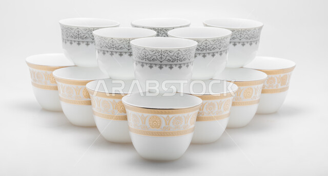 اكواب بيضاء مزخرفة باللون الذهبي والفضي، صورة مقربة لمجموعة من الفناجين الصغيرة، فنجان ضيافة صغير، أكواب زجاجية صغيرة لتقديم المشروبات الساخنة، خلفية بيضاء