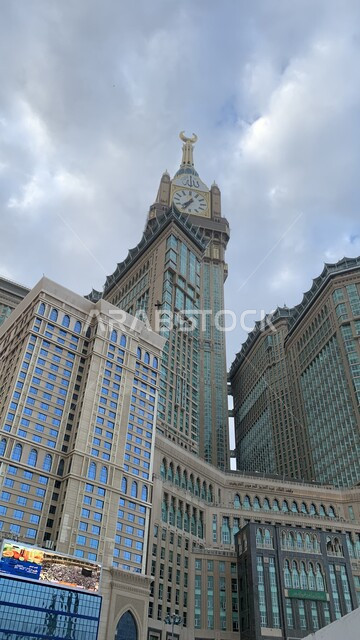 الفن الهندسي المعماري لناطحات السحاب، معالم دينية إسلامية مقدسة، صورة من الاسفل لمبنى برج الساعة الملكي في مكة المكرمة، العبادة والتقرب إلى الله، الأبراج المطلة على الحرم المكي الشريف في المملكة العربية السعودية ،منظر السماء الملبدة بالغيوم