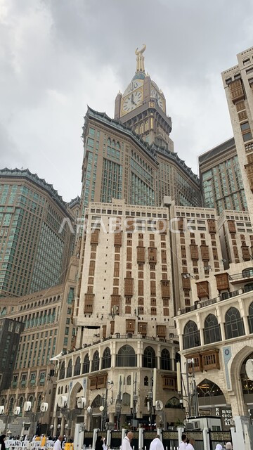 العبادة والتقرب إلى الله، مبنى برج الساعة الملكي في مكة المكرمة، الفن الهندسي المعماري لناطحات السحاب، معالم دينية إسلامية مقدسة، صورة مقربة لحجاج بيت الله الحرام في الحرم المكي الشريف في المملكة العربية السعودية، منظر السماء الملبدة بالغيوم