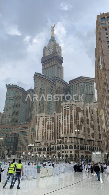 مبنى برج الساعة الملكي في مكة المكرمة، الفن الهندسي المعماري لناطحات السحاب، معالم دينية إسلامية مقدسة، صورة مقربة لحجاج بيت الله الحرام في الحرم المكي الشريف في المملكة العربية السعودية، العبادة والتقرب إلى الله، منظر السماء الملبدة بالغيوم