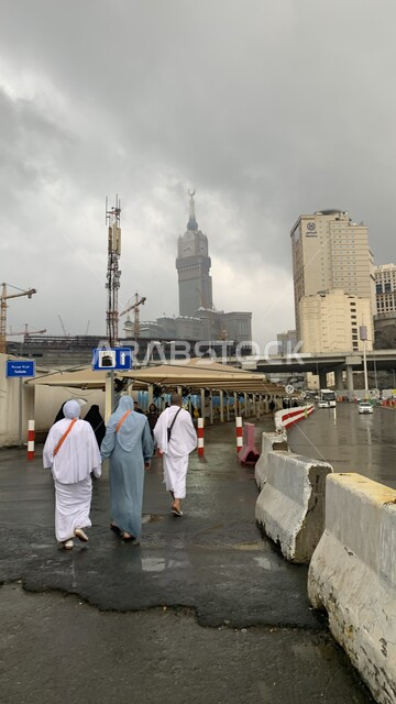 مبنى برج الساعة الملكي في مكة المكرمة، صورة من الخلف لحجاج بيت الله الحرام في الحرم المكي الشريف في السعودية، الفن الهندسي المعماري لناطحات السحاب، أسلوب الحياة في المملكة، العبادة والتقرب إلى الله، منظر السماء الملبدة بالغيوم