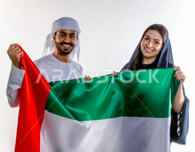 زوجان اماراتيان  يحتفلان باليوم الوطني لدولة الامارات العربية المتحدة ، يحملان علم دولة الامارات مع ايماءات وجه تدل ل الحب و السعادة  ،  ذكرى اليوم الوطني الاماراتي ، يوم الاستقلال ، الوطني الاماراتي