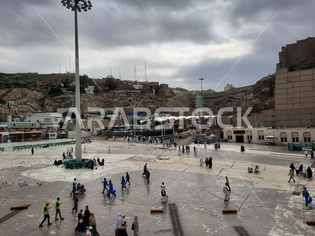 الاهتمام بنظافة الحرم المكي الشريف في السعودية، طواقم التنظيف في الساحات الخارجية لبيت الله الحرام، اماكن اسلامية مقدسة، المسجد الحرام في مكة المكرمة، الحجاج والمسلمين في ساحات الحرم المكي، معالم دينية إسلامية، خلفية السماء الملبدة بالغيوم