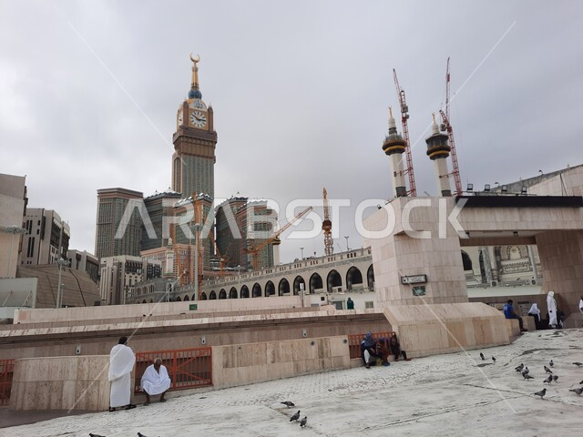 Performing worship and getting closer to God, luxury hotels and towers surrounding the mosque, sacred Islamic religious places and landmarks, the Royal Clock Tower in Mecca, a destination for Muslims from various countries, the background of the cloudy sky