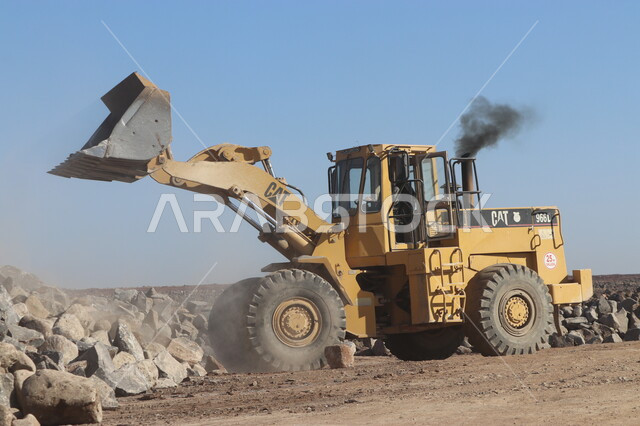 جرافة تعمل على رفع وتعبئة الرمال والحصى، مفهوم الهندسة والبناء والتطوير، مهن ووظائف هندسية في السعودية، معمل تكسير الحجارة والآلات الضخمة، قوة وتقنية عملية استخراج وتحطيم الصخور، آلات ومعدات ثقيلة