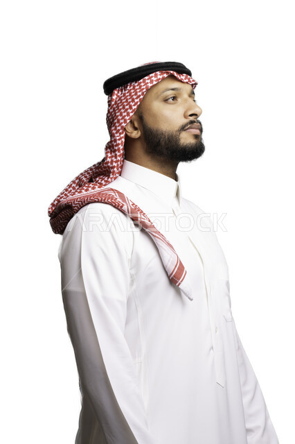 التركيز والتأمل لحل المشكلات, مفهوم التردد والحيرة، التخطيط والتفكير لاتخاذ القرارات، الأناقة والاهتمام بالمظهر الخارجي، بورتريه لشاب عربي خليجي سعودي يرتدي الشماغ والثوب التقليدي ينظر الى شيء ما ، إيماءات الجدية والحزم, خلفية بيضاء .
