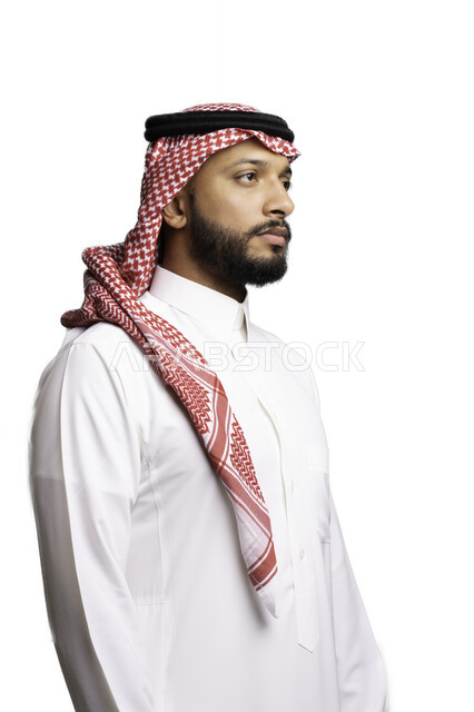 التركيز والتأمل لحل المشكلات, مفهوم التردد والحيرة، التخطيط والتفكير لاتخاذ القرارات، الأناقة والاهتمام بالمظهر الخارجي، بورتريه لشاب عربي خليجي سعودي يرتدي الشماغ والثوب التقليدي ينظر الى شيء ما ، إيماءات الجدية والحزم, خلفية بيضاء .