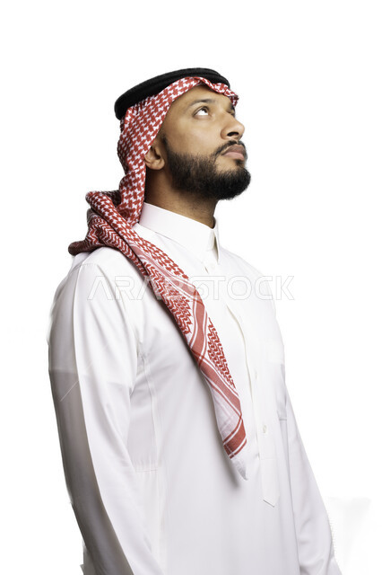 التفكير والتخطيط لحل مشكلة ما، التأمل والتركيز لاتخاذ القرارات, مفهوم التردد والحيرة، الأناقة والاهتمام بالمظهر الخارجي، بورتريه لشاب عربي خليجي سعودي يرتدي الشماغ والثوب التقليدي ينظر الى شيء ما في الأعلى، خلفية بيضاء .