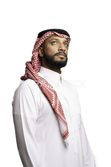 التأمل والتركيز لاتخاذ القرارات, مفهوم التردد والحيرة، التخطيط والتفكير لحل مشكلة ما، الأناقة والاهتمام بالمظهر الخارجي، بورتريه لشاب عربي خليجي سعودي يرتدي الشماغ والثوب التقليدي ينظر الى شيء ما في الأعلى، خلفية بيضاء .