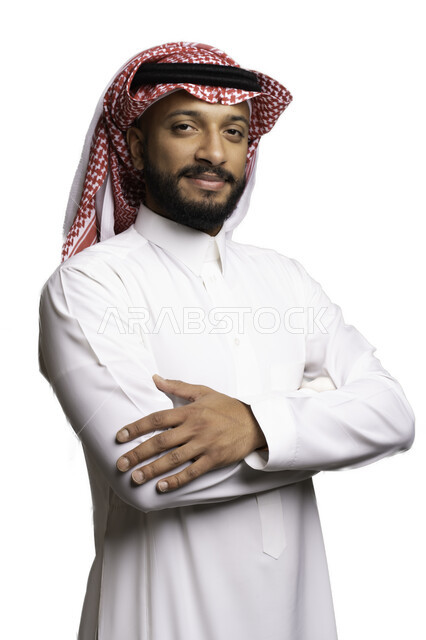 Gestures of happiness and joy, elegance and attention to external appearance, the concept of handsomeness and masculinity, a close-up portrait of a smiling Saudi Gulf Arab man wearing a shemagh and traditional dress, standing with crossed hands looking at the camera with expressions of pleasure and self-confidence, white background