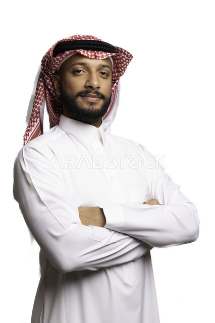 الأناقة والاهتمام بالمظهر الخارجي، مفهوم الوسامة والرجولة، التقاط صور شخصية للوثائق الرسمية، بورتريه مقرب لرجل عربي خليجي سعودي مبتسم يرتدي الشماغ والثوب التقليدي يقف بأيدي متقاطعة ينظر الى الكاميرا بتعابير السرور والثقة بالنفس، خلفية بيضاء .