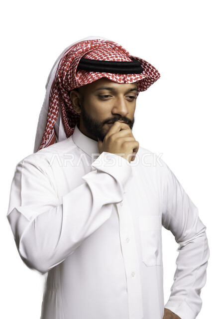 إيماءات التفكير والحيرة، مفهوم الاناقة والرجولة، بورتريه مقرب لشاب عربي خليجي سعودي مبتسم يرتدي الشماغ والثوب التقليدي ينظر الى شيء ما بالتمعن والتركيز لاتخاذ القرارات، الأناقة والاهتمام بالمظهر الخارجي، إيجاد الحلول للمشكلات، خلفية بيضاء .