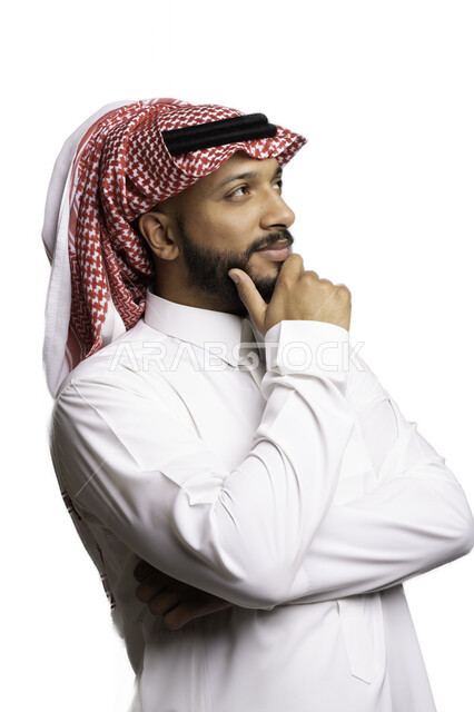التركيز والتمعن لاتخاذ القرارات، مفهوم الاناقة والرجولة، بورتريه مقرب لشاب عربي خليجي سعودي مبتسم يرتدي الشماغ والثوب التقليدي يضع يده تحت رأسه ينظر الى شيء ما بإيماءات التفكير والحيرة، الأناقة والاهتمام بالمظهر الخارجي، إيجاد الحلول للمشكلات، خلفية بيضاء .