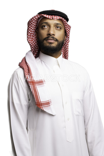 Elegance and attention to external appearance, thinking and planning to solve a problem, contemplating and focusing to make decisions, the concept of confusion and hesitation, a portrait of a Saudi Gulf Arab young man wearing a shemagh and traditional dress, looking at something with gestures of contemplation and absent-mindedness, a white background