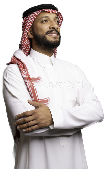 Gestures of thought and absent-mindedness, contemplation and looking at something, the concept of elegance and masculinity, a close-up portrait of a smiling Saudi Gulf Arab man wearing a shemagh and traditional dress, standing with crossed hand movements, taking care and attention to his external appearance, a white background