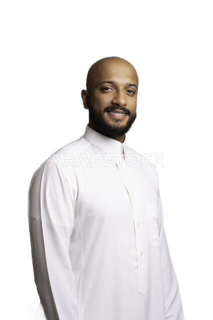 إيماءات السرور والثقة بالنفس، الاعتناء والاهتمام بالمظهر الخارجي، مفهوم الاناقة والرجولة، التقاط صور شخصية للوثائق الرسمية، بورتريه مقرب لشاب عربي خليجي سعودي أصلع مبتسم يرتدي الثوب التقليدي يقف باستقامة ينظر الى الكاميرا، خلفية بيضاء .
