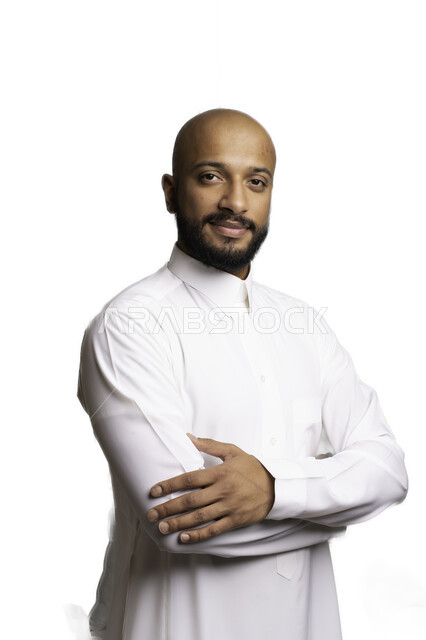 الاهتمام والاعتناء بالمظهر الخارجي، مفهوم الاناقة والرجولة، التقاط صور شخصية للوثائق الرسمية، بورتريه مقرب لشاب عربي خليجي سعودي أصلع مبتسم يرتدي الثوب التقليدي يقف بأيدي متقاطعة ينظر الى الكاميرا بتعابير السرور والثقة بالنفس، خلفية بيضاء .
