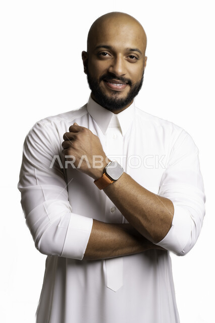 الاعتناء والاهتمام بالمظهر الخارجي، مفهوم الاناقة والرجولة، التقاط صور شخصية للوثائق الرسمية، بورتريه مقرب لشاب عربي خليجي سعودي أصلع مبتسم يرتدي الثوب التقليدي وساعة يد ينظر الى الكاميرا بتعابير السرور والثقة بالنفس، خلفية بيضاء