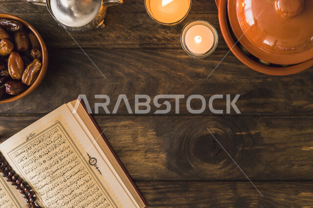 صورة علوية للقران الكريم مفتوح قرب طبق من التمر والشموع المشتعلة، العبادة والتقرب الى الله، وجبة ذات قيمة غذائية عالية، أجود أنواع التمور الصحية واللذيذة