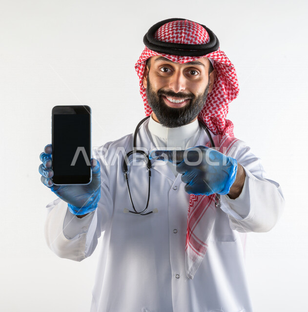 بورتريه لطبيبب سعودي خليجي مبتسم و يستخدم هاتفه المحمول  ،  الاتصال و التواصل عن بعد ، يقدم خدماته للمرضى بكل كفاءه  ، خلفية بيضاء، مفهوم الطب والرعاية الصحية