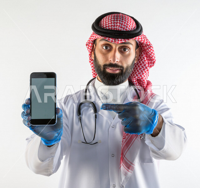 بورتريه لطبيبب سعودي خليجي مبتسم و يستخدم هاتفه المحمول  ،  الاتصال و التواصل عن بعد ، يقدم خدماته للمرضى بكل كفاءه  ، خلفية بيضاء، مفهوم الطب والرعاية الصحية