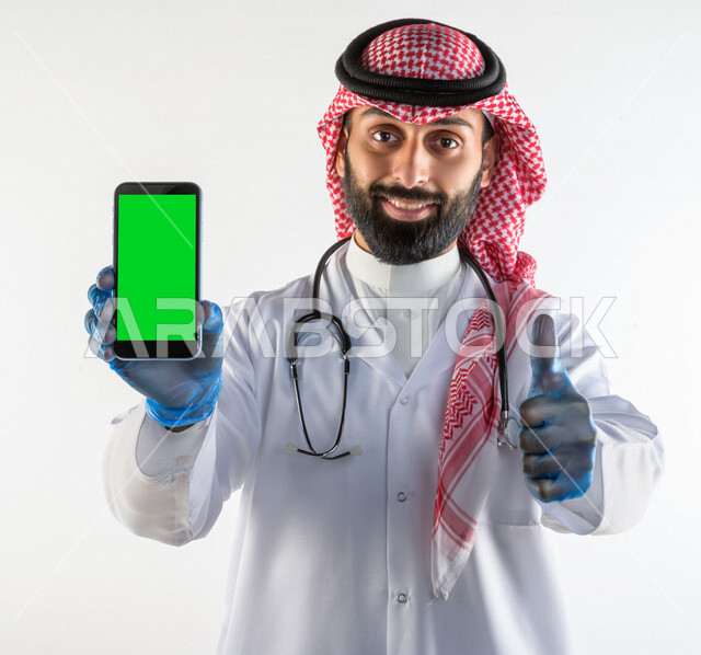 بورتريه لطبيبب سعودي خليجي مبتسم و يستخدم هاتفه المحمول بخلفية خضراء كروما  ،  الاتصال و التواصل عن بعد ، يقدم خدماته للمرضى بكل كفاءه  ، خلفية بيضاء، مفهوم الطب والرعاية الصحية