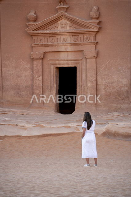 التكوين والتشكيل الصخري في مناطق القمم والمرتفعات الجبلية, صورة من الخلف لسائحة عربية خليجية تستمتع في مدائن صالح في محافظة العلا التراثية,  أماكن الجذب السياحي من شتى أنحاء العالم, السياحة في المناطق الصحراوية, الحضارة والآثار العربية التاريخية القديمة, معالم سياحية مشهورة