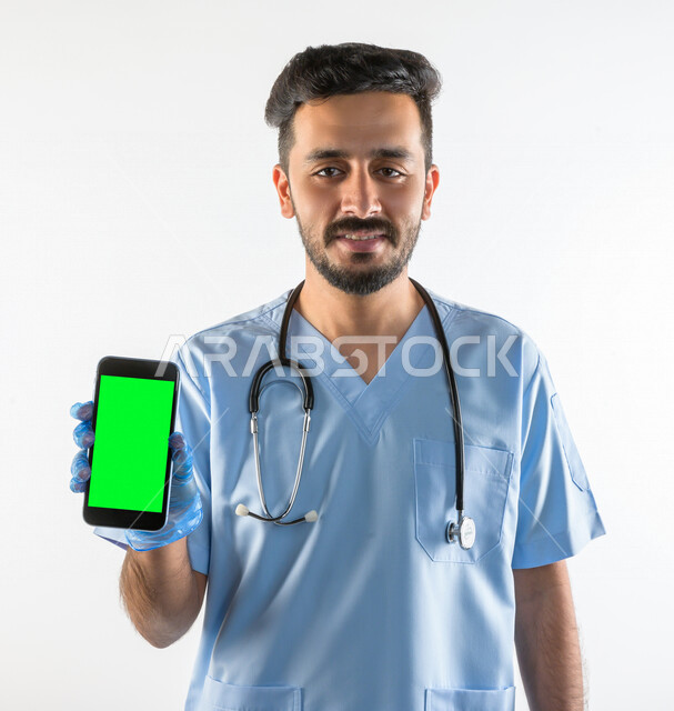 بورتريه لطبيبب سعودي خليجي مبتسم و يستخدم هاتفه المحمول بخلفية خضراء كروما  ،  الاتصال و التواصل عن بعد ، يقدم خدماته للمرضى بكل كفاءه  ، خلفية بيضاء، مفهوم الطب والرعاية الصحية