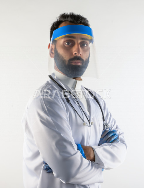 طبيبب سعودي يرتدي معدات وقائية لمكافحة فيروس كورونا   ، يرتدي قناع الوجه ، القناع البلاسيتكي الوقائي ، اتباع اجراءات السلامة  ، تجنب انتشار العدوى ، خلفية بيضاء، مفهوم الطب والرعاية الصحية