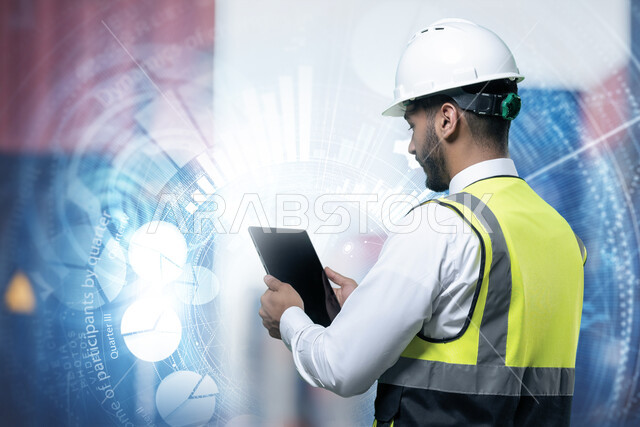 Follow up and supervise the work via the tablet, a picture from the back of a Saudi Arabian Gulf Arab supervisory engineer wearing a helmet and a protective vest inside the factory, technological development and progress in the field of industry and engineering, a graphic lens background with hologram technology.