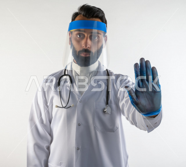 طبيبب سعودي يرتدي معدات وقائية لمكافحة فيروس كورونا   ، يرتدي قناع الوجه ، القناع البلاسيتكي الوقائي ، اتباع اجراءات السلامة  ، تجنب انتشار العدوى ، خلفية بيضاء، مفهوم الطب والرعاية الصحية