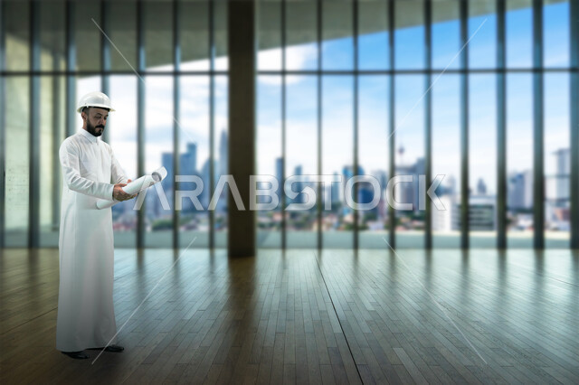 Working in the engineering sector, the concept of engineering and construction, supervising the implementation of architectural plans and projects in Saudi Arabia, a Saudi Gulf Arab engineer wearing a traditional dress and wearing a protective helmet, holding a building plan in his hand, standing at his workplace.